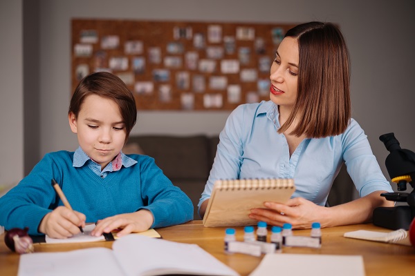 Aunt and nephew do homework together. Women explain kid writes in notebook. Schoolboy studying at home. Family relationships, primary education, childhood