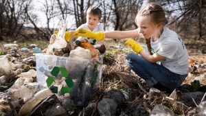 Boy and girl collecting plastic garbage in a container in a polluted clearing, recycling signs on the T-shirts