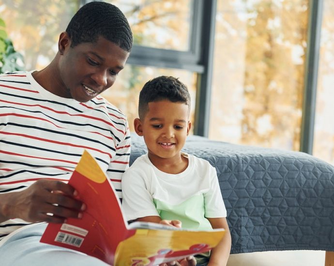African American father with his young son at home, reading