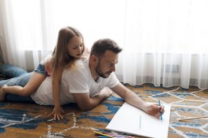 Father writing on notebook as a girl watches.