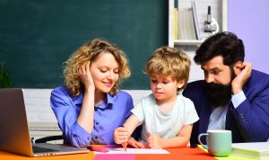 A female teacher, a boy, and his father in a classroom.