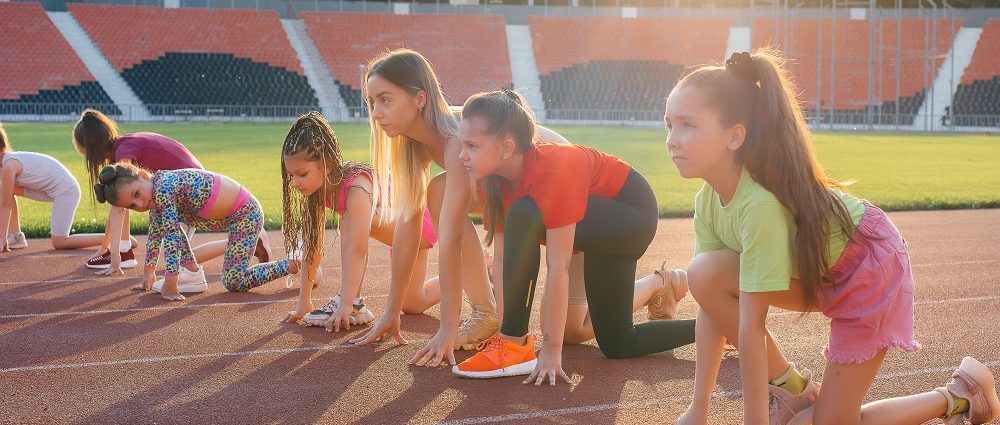 A large group of girls, are taught by a coach at the start before running at the stadium during sunset. A healthy lifestyle.