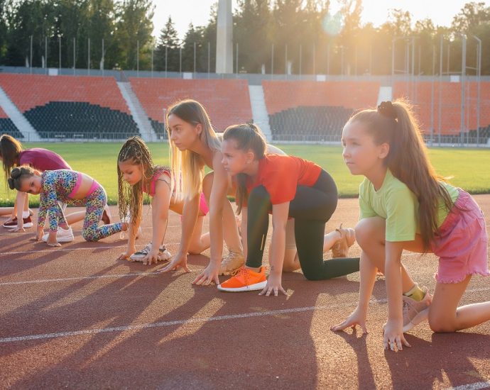 A large group of girls, are taught by a coach at the start before running at the stadium during sunset. A healthy lifestyle.