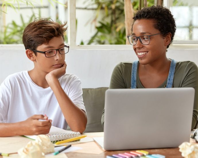 Self education and e learning concept. Satisfied black female volunteer tries to explain her strategy to young learner, watch attentively video in laptop computer. Tutor teaches skilled student