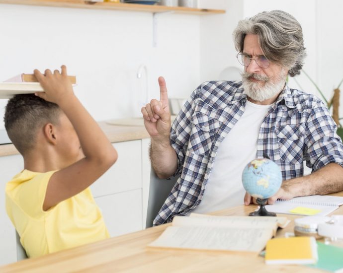 A child holding a book on his head while his father is admonishing him