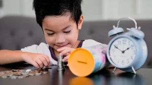 A boy counting coins with clock on the table.