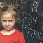 A girl upset in front of blackboard showing math