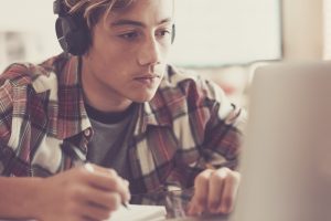Portrait up of caucasian teenager with headphones staring at laptop screen during playing computer games, chatting on the Internet or viewing videos. - Image