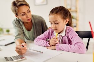 Young mother explaining mathematic to her daughter while homeschooling during virus epidemic. Focus is on girl.