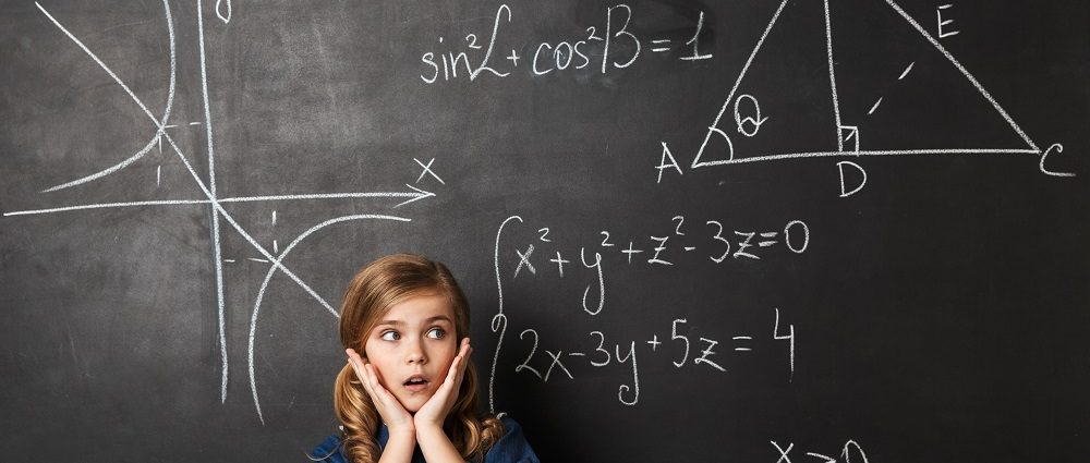 Smart little schoolgirl standing at the blackboard with math graphics written on it