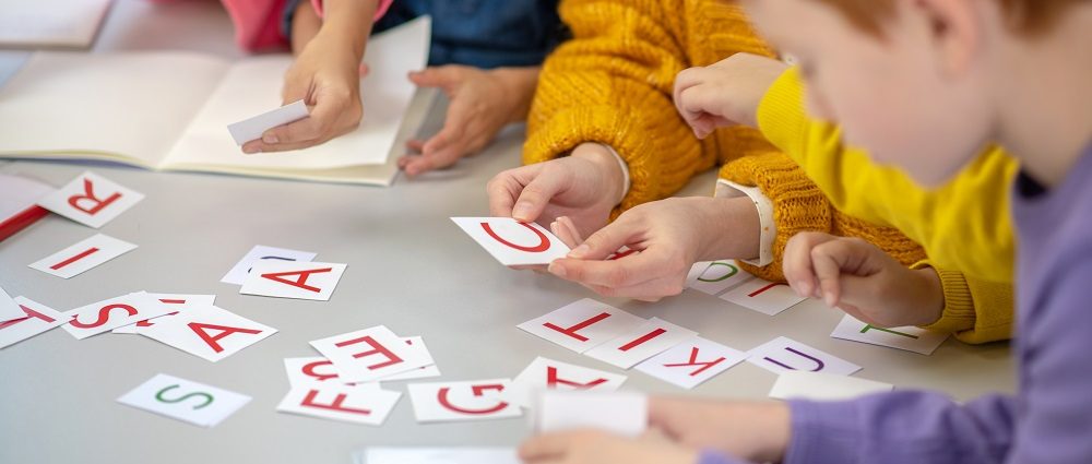 Learning letters. Close up picture of a school desk with different cards on it and children sitting around