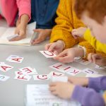 Learning letters. Close up picture of a school desk with different cards on it and children sitting around