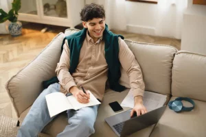 A male student using laptop and taking notes